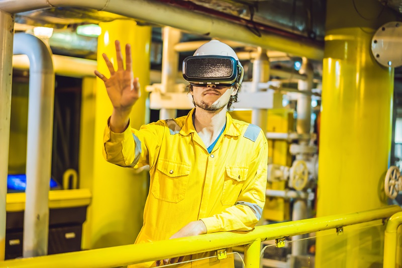 Young man in a yellow work uniform, glasses and helmet uses virtual reality glasses in industrial environment,oil Platform or liquefied gas plant.
